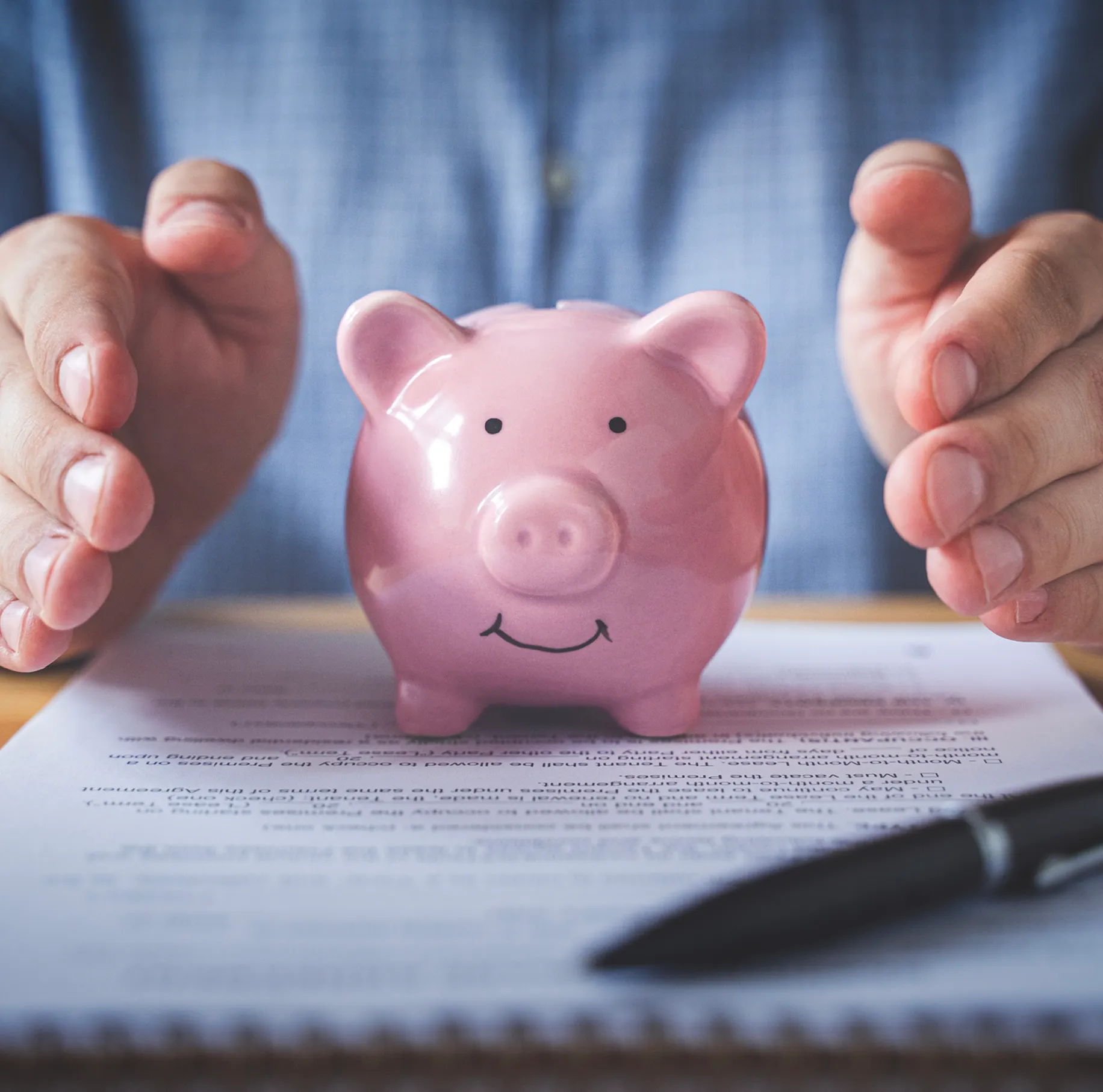 Hands protecting a pink piggy bank.